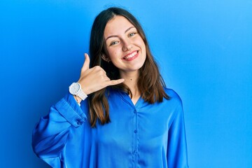 Young brunette woman wearing casual blue shirt smiling doing phone gesture with hand and fingers like talking on the telephone. communicating concepts.