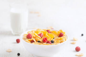 bowl of corn granola with milk, fresh raspberries, blueberries . milk in a jug and a glass  on white wooden board for healthy breakfast