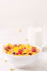 bowl of corn granola with milk, fresh raspberries, blueberries . milk in a jug and a glass  on white wooden board for healthy breakfast