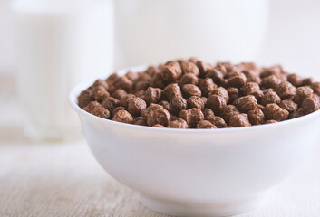 Bowl with chocolate corn balls and milk, on white wooden background.