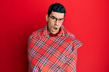 Fototapeta premium Handsome hispanic man wrapped in a red warm red blanket in shock face, looking skeptical and sarcastic, surprised with open mouth