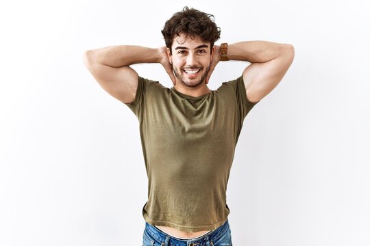 Hispanic man standing over isolated white background relaxing and stretching, arms and hands behind head and neck smiling happy