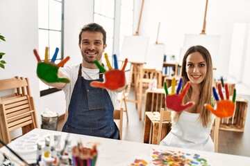 Two hispanic students smiling happy showing colorulf painted hands at art studio.