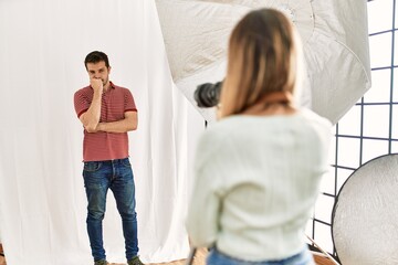 Woman photographer talking pictures of man posing as model at photography studio looking stressed and nervous with hands on mouth biting nails. anxiety problem.