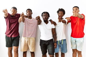 Young african group of friends standing together over isolated background pointing with finger surprised ahead, open mouth amazed expression, something on the front