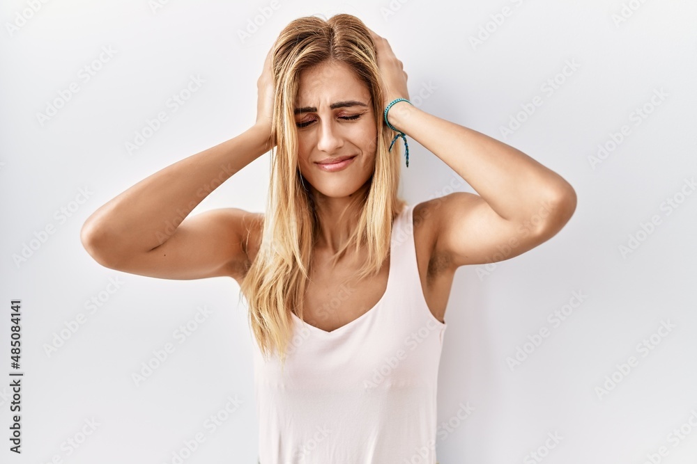 Poster blonde beautiful young woman standing over white isolated background suffering from headache despera