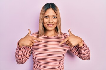 Beautiful hispanic woman wearing casual striped sweater looking confident with smile on face,...
