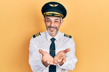Handsome middle age man with grey hair wearing airplane pilot uniform smiling with hands palms...