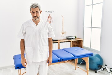 Obraz premium Middle age hispanic therapist man working at pain recovery clinic skeptic and nervous, frowning upset because of problem. negative person.