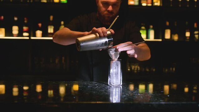 Professional bartender creating a cocktail drink. Bartender is preparing an alcoholic cocktail with ice cubes to customers at the bar. Night life