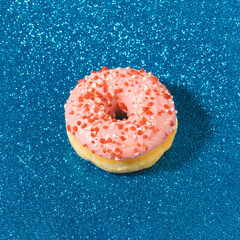 Creative composition with single pink donut on blue glitter  background. Minimal luxury pastry concept.