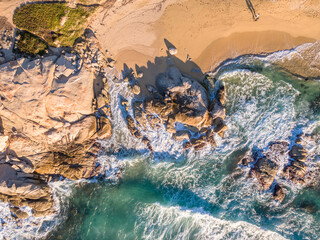 Aerial view of two people walking past rocks along a sandy beach at Aregno Plage near Algajola in the Balagne region of Corsica