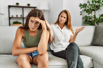 Mother and daughter unhappy arguing sitting on sofa at home