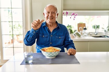 Senior man with grey hair eating pasta spaghetti at home showing and pointing up with finger number one while smiling confident and happy.