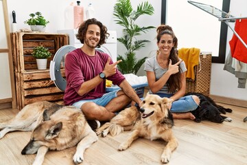 Young hispanic couple doing laundry with dogs cheerful with a smile on face pointing with hand and finger up to the side with happy and natural expression
