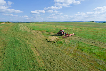 Naklejka premium A red tractor rakes the mown grass for drying. Modern equipment on the field.