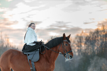 Obraz premium A girl in a white cloak rides a brown horse in winter.