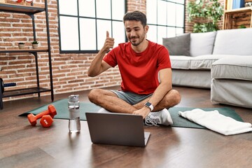 Young hispanic man watching training tutorial at home smiling happy and positive, thumb up doing excellent and approval sign