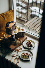 a birthday cake and two plates of sliced cake. cake on the windowsill near the window. biscuit cake with caramel and blueberries on top top view