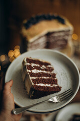 A piece of biscuit cake on a plate. hold a plate with a chocolate cake with cream cheese. Dark crude with white cream