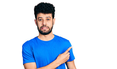 Young arab man with beard wearing casual blue t shirt pointing aside worried and nervous with...