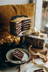a birthday cake and two plates of sliced cake. cake on the windowsill near the window. biscuit cake with caramel and blueberries on top top view	
