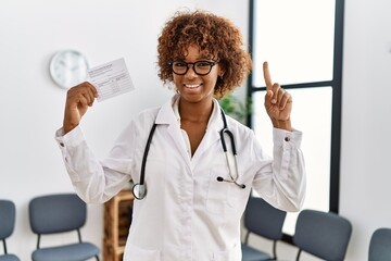 Young african american doctor woman holding covid record card smiling with an idea or question...
