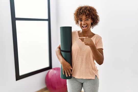 Young african american woman holding yoga mat at pilates room smiling happy pointing with hand and finger