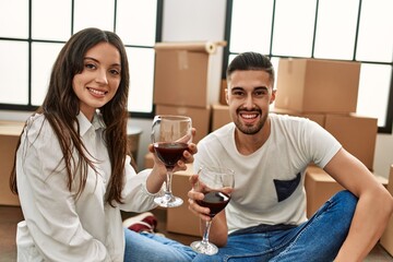 Young hispanic couple smiling happy toasting with red wine at new home.