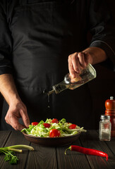 Professional chef pours oil into a salad bowl in the kitchen. Cooking delicious and healthy food with a set of vitamins
