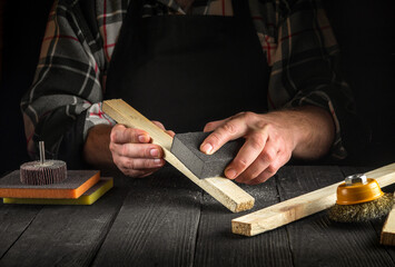 Woodworker cleans wooden planks with an abrasive tools. Hands of the builder close-up during work. Renovation or construction idea