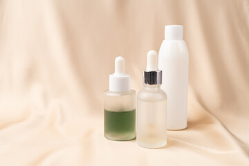 Fototapeta na wymiar Jars of serum with a dropper for moisturizing the skin of the face and a white bottle of tonic on a nude creamy silk fabric. Skin care.