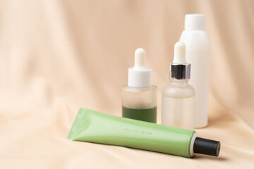 Jars of serum with a dropper for moisturizing the skin of the face, a white bottle of tonic and an anti-aging eye cream on a nude creamy silk fabric. Skin care