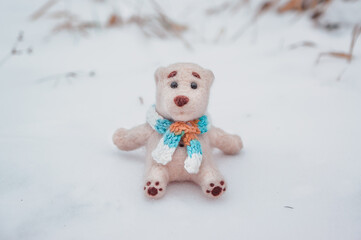 a toy polar bear in a scarf sits on the snow and looks at the camera
