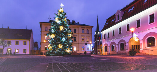 Fototapeta premium A deserted square photographed at night in the dark. The lights of Christmas decorations shine all around. There is a decorated Christmas tree in the square.