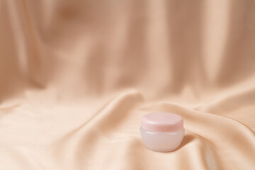 Moisturizing anti-aging face cream on a nude pink silk fabric. Skin care.