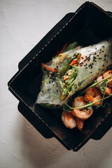 a portion of shrimp and spring rolls with fresh vegetables. healthy food in a paper plate on a white background. food delivery and takeaway top view. sports nutrition for muscles and weight loss