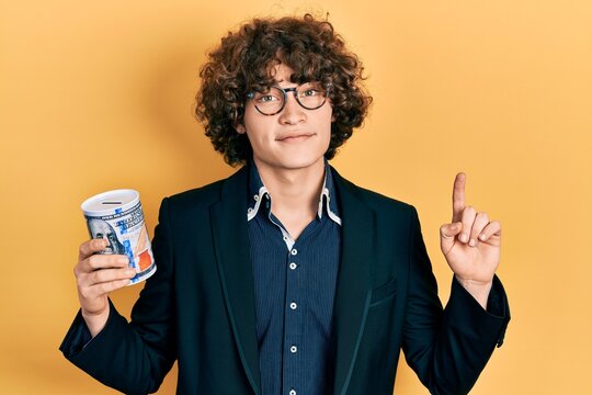 Handsome young man holding piggy bank surprised with an idea or question pointing finger with happy face, number one