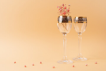 Two beautiful glass goblets on a high stem with golden edges and flowers inside on a nude cream fabric