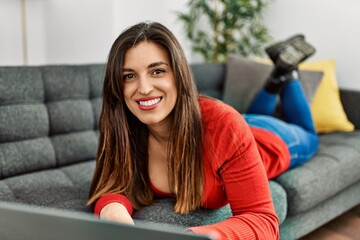 Obraz premium Young woman using laptop lying on sofa at home