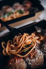 eating food from delivery or food to go. pasta with tomato sauce and round meatballs in a paper bowl. black fork with pasta.