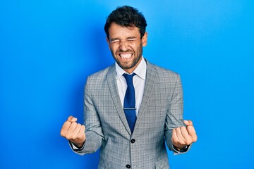 Handsome man with beard wearing business suit and tie very happy and excited doing winner gesture with arms raised, smiling and screaming for success. celebration concept.