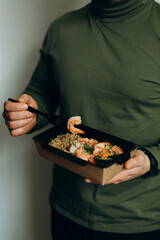 a man in a green sweater eats shrimp with a side dish in a paper plate. food delivery or takeaway. lunch during lunch break close-up.	
