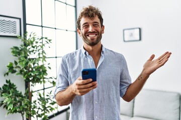 Young handsome man using smartphone at home celebrating achievement with happy smile and winner expression with raised hand