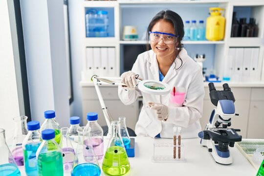 Young chinese woman wearing scientist uniform using loupe at laboratory