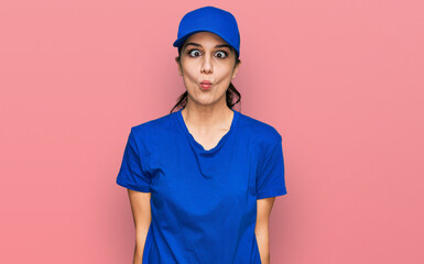 Young hispanic girl wearing delivery courier uniform making fish face with lips, crazy and comical gesture. funny expression.