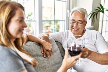 Middle age hispanic couple smiling happy drinking wine sitting on the sofa at home.