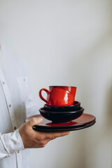 a man in a white shirt holds a set of red ceramic dishes in his hands. set of designer handmade ceramic kitchen utensils. plates of different sizes and cups.	
