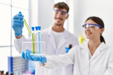 Man and woman partners wearing scientist uniform holding test tube at laboratory