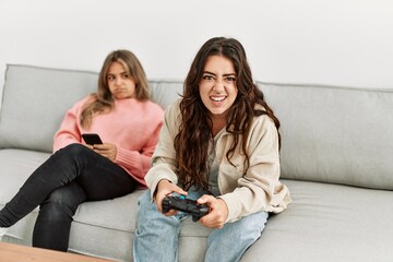 Girl playing video game and her girlfriend boring using smartphone at home.